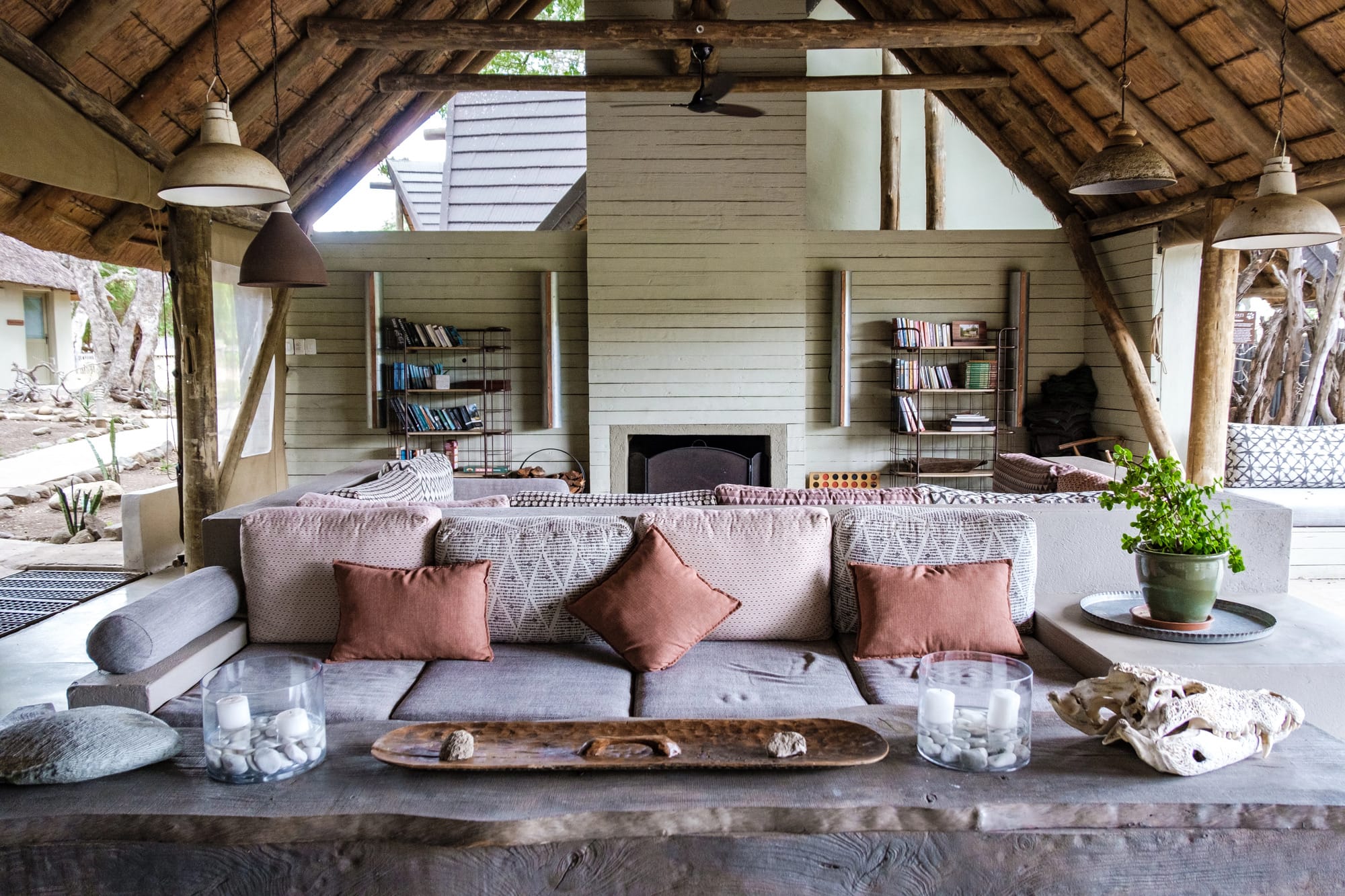 An open-sided thatched lounge with deep sofas, a fireplace and bookshelves