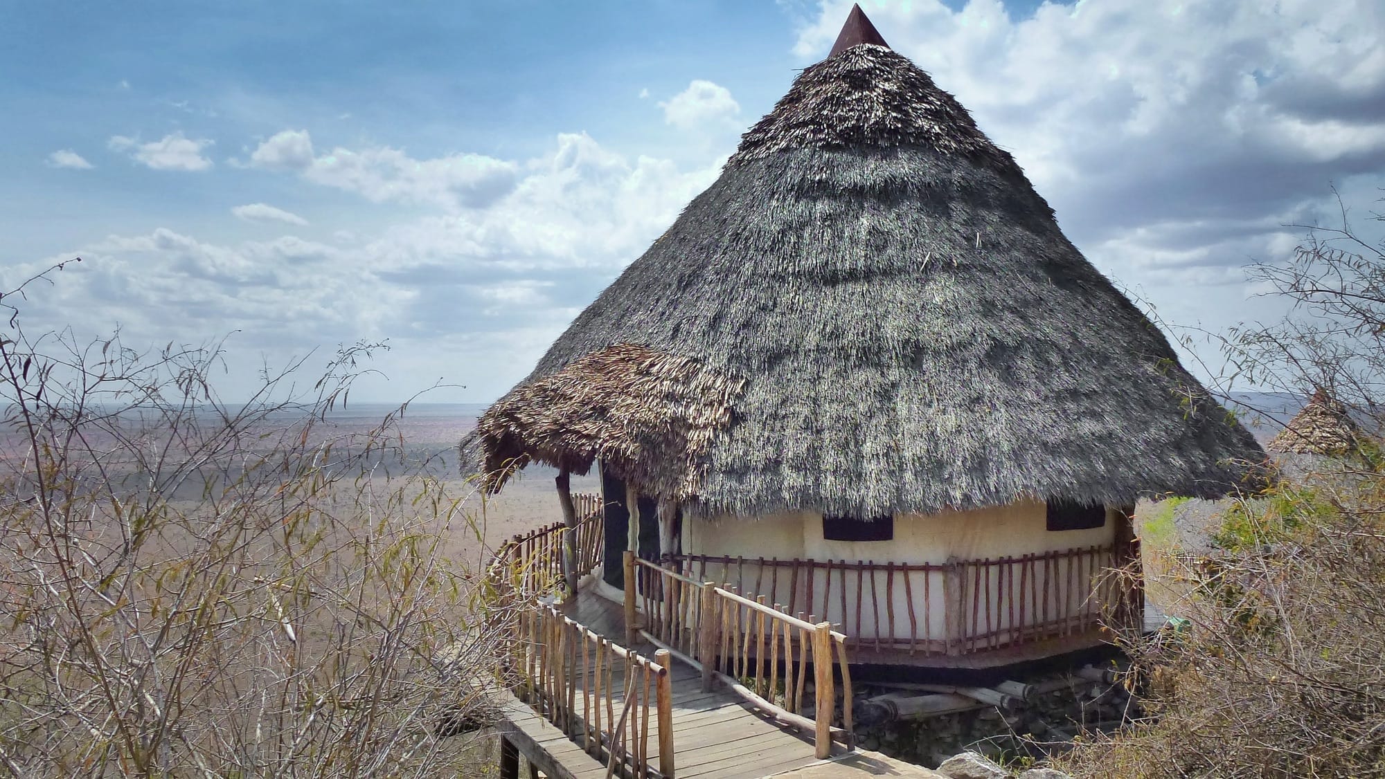 A round thatched banda on a ridge, reached by a boardwalk, looking out over dry plains