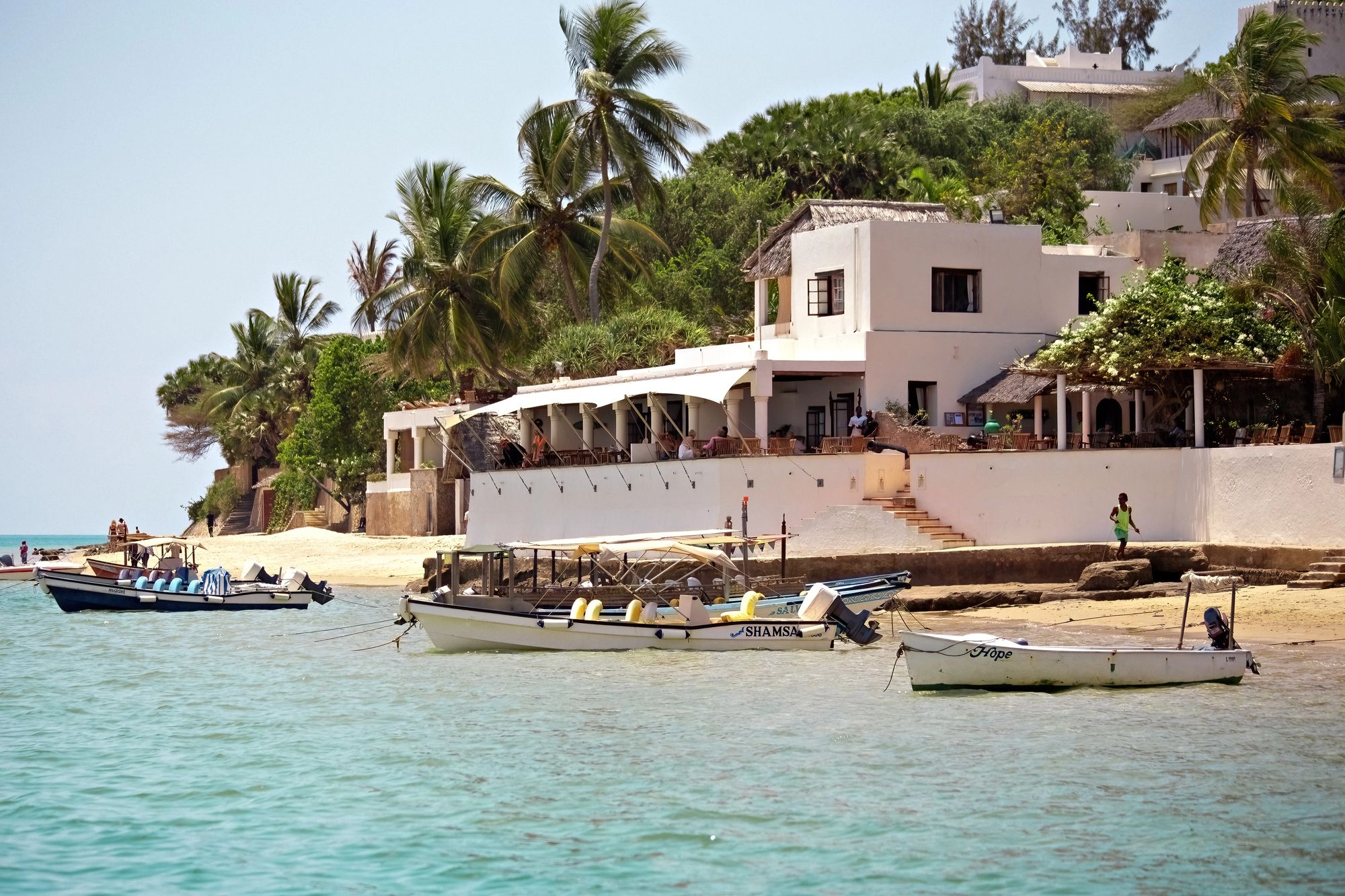 A whitewashed Swahili-coast hotel above the beach, with boats moored offshore
